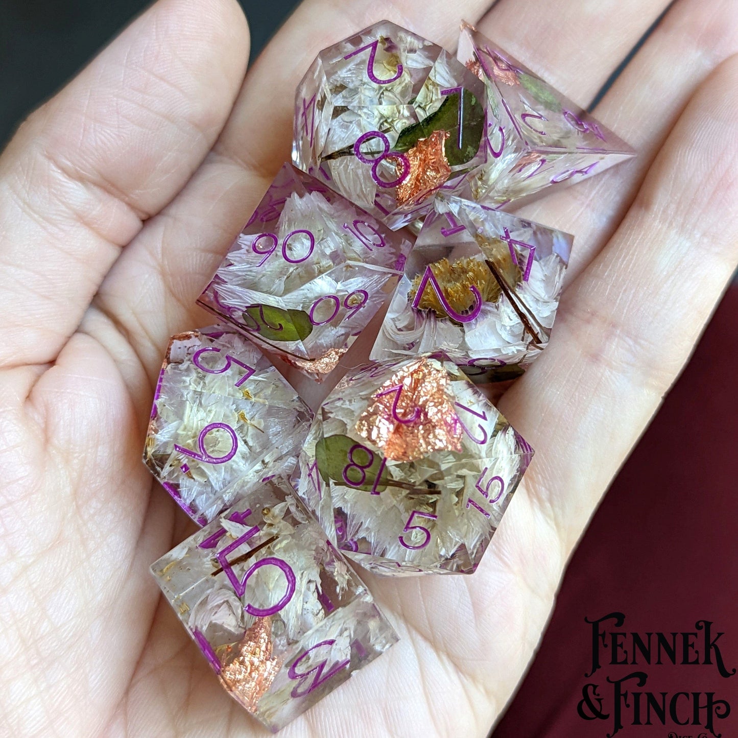 Hand holding Magenta Ink Daisy Sharp Edge DnD Dice Set with daisies, leaves, and copper foil, showcasing resin's glass-like finish.