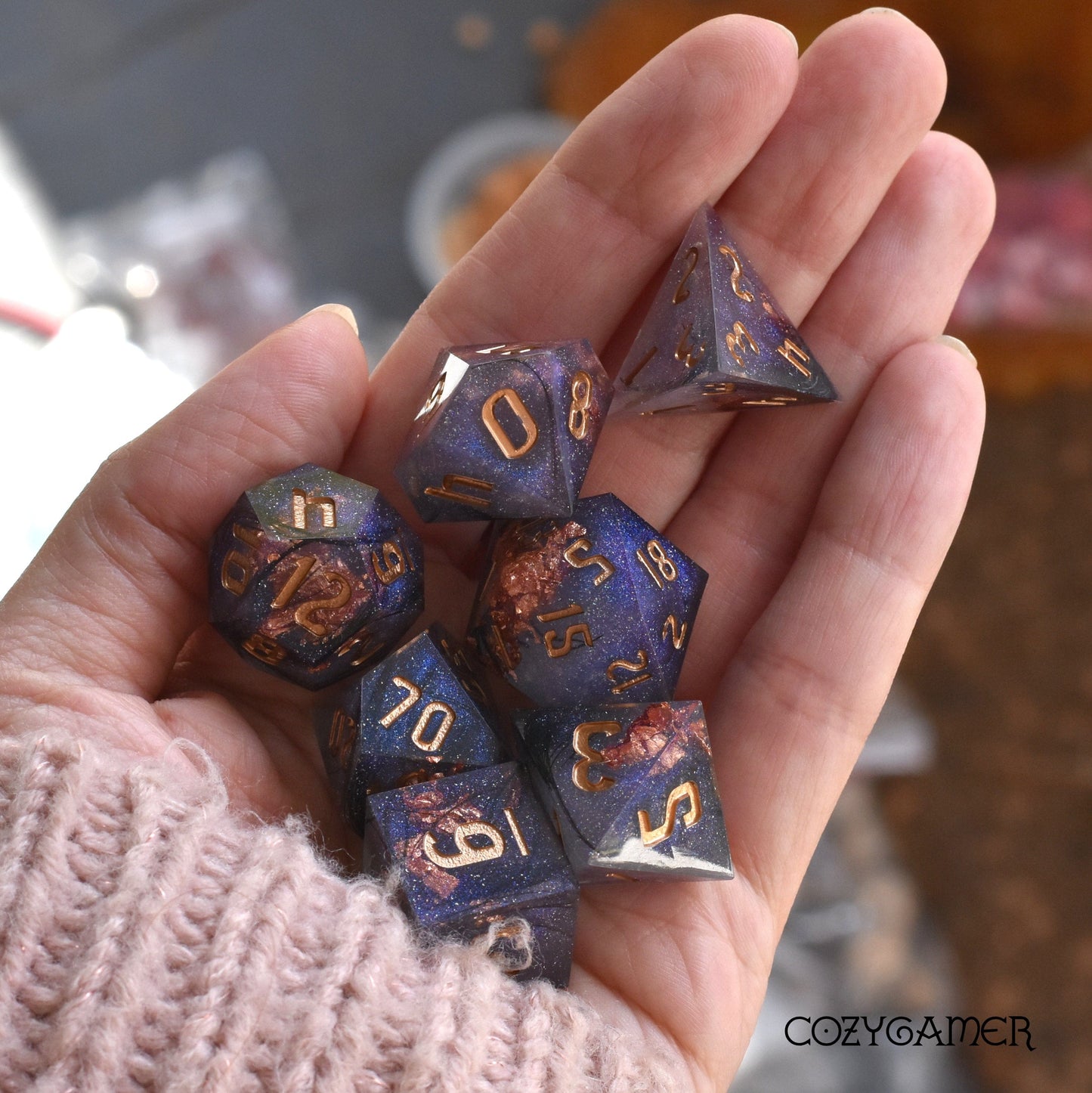 Hand holding Magic Feather sharp edge resin DnD dice set with black feathers, copper foil, and glitter for tabletop games.