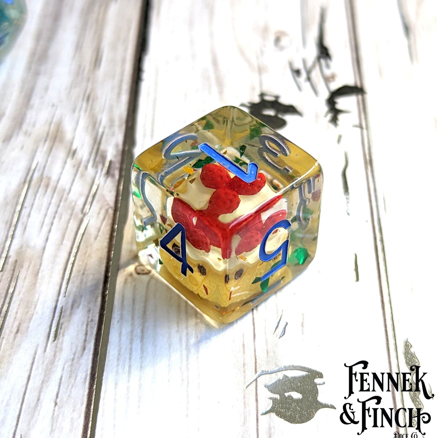 Large pastry dice with red miniature cake inside for tabletop games like Dungeons and Dragons, featuring blue numbers.