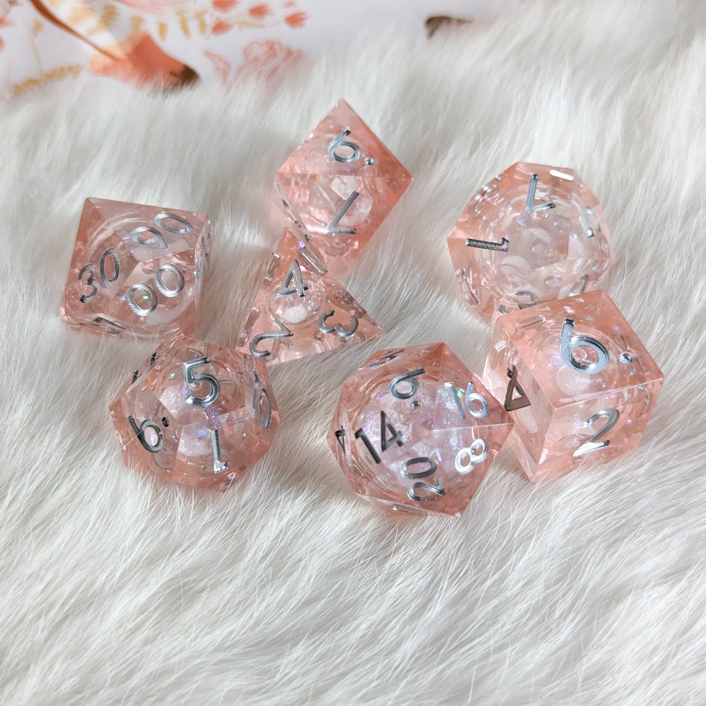 Peach Liquid Core Sharp Edge Resin DnD Dice Set with shimmer on a fluffy white surface.