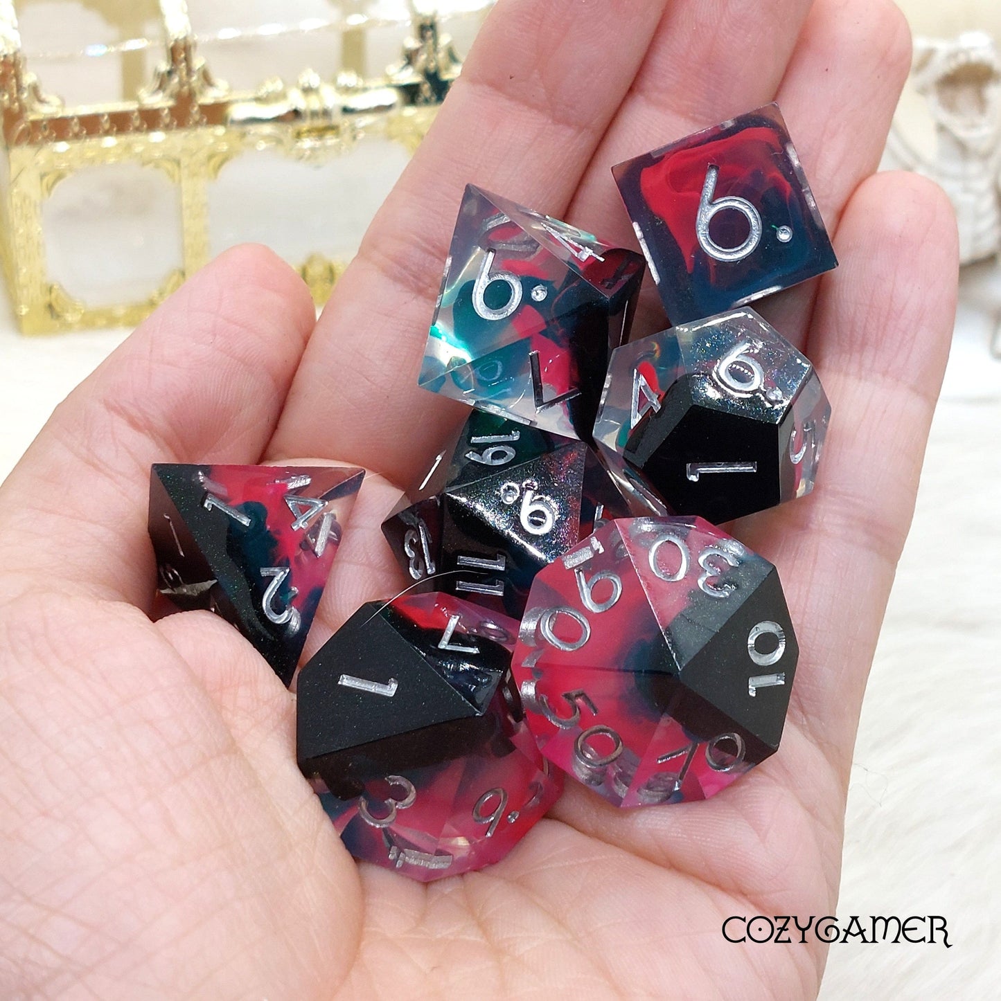 Hand holding Perfect Weapon sharp edge resin dice set with black, pink, and blue swirling flames, 7 piece polyhedral TTRPG dice.