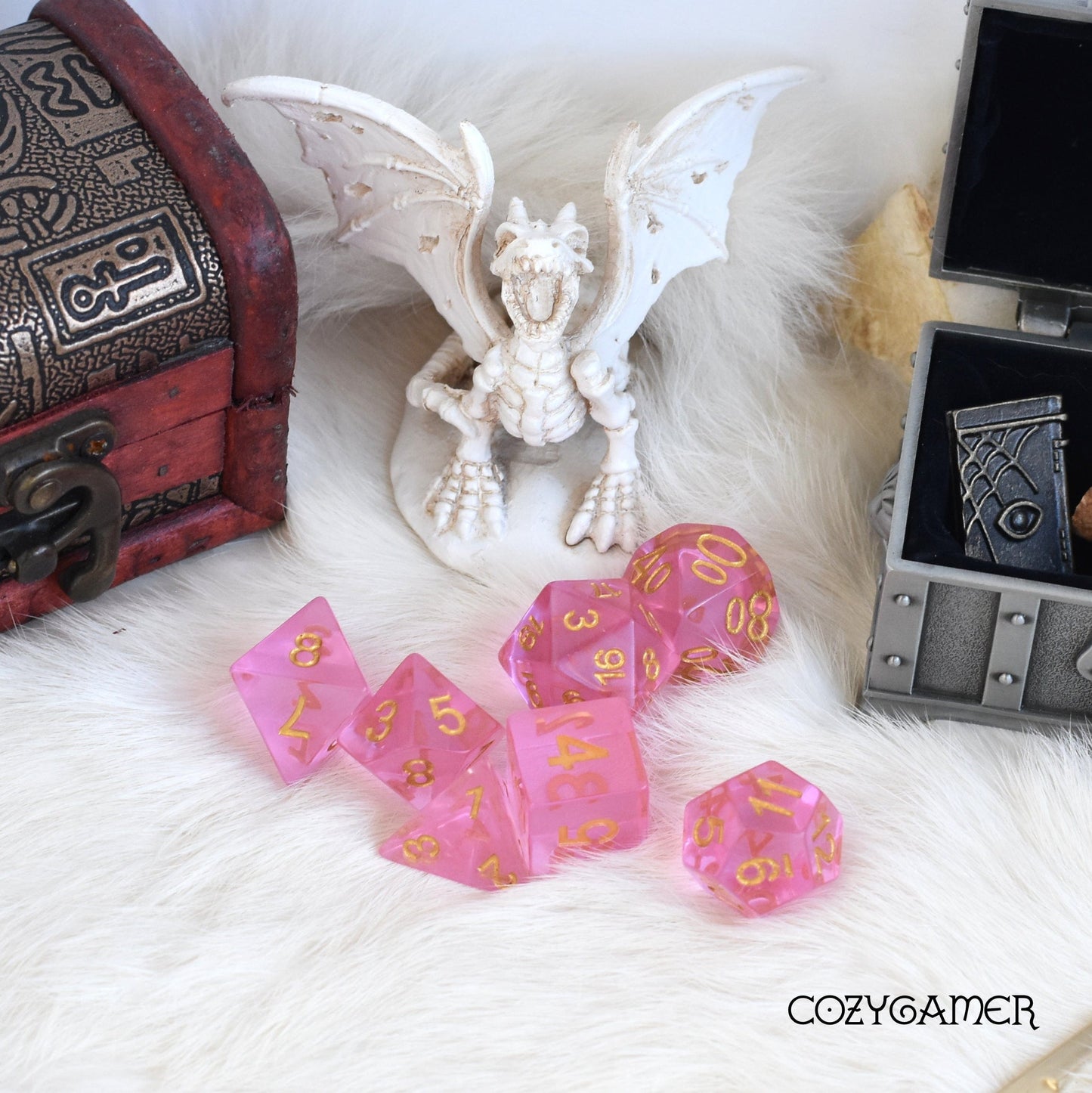 Pink Crystal Dice Set with gold numbers, next to dragon figurine and treasure chest, perfect for tabletop role-playing games.