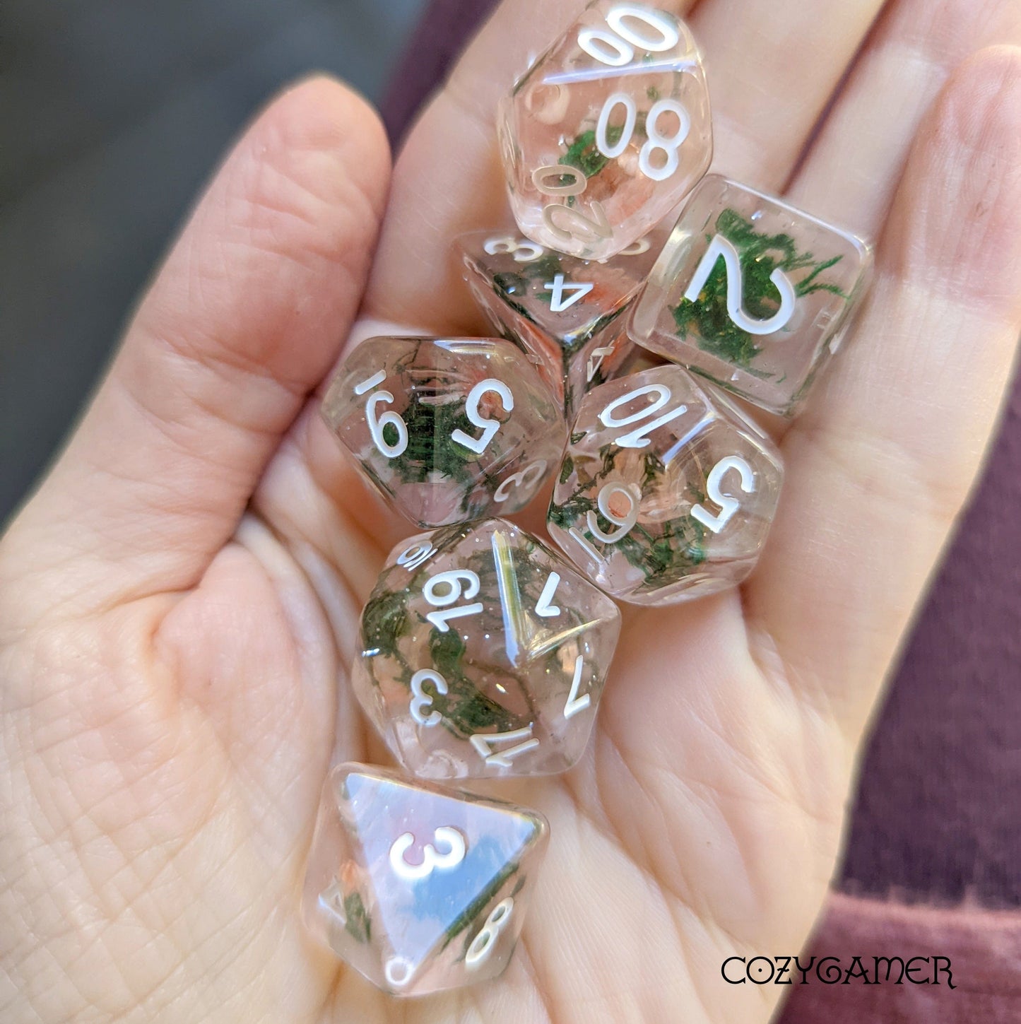 Hand holding Pink Flower and Moss Dice Set with real dried plants in clear resin for tabletop RPGs like DnD.