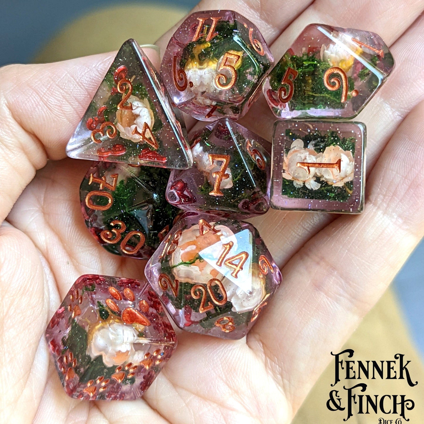 Hand holding pink flowers and moss DnD dice set with dried flowers in glittering pink resin.