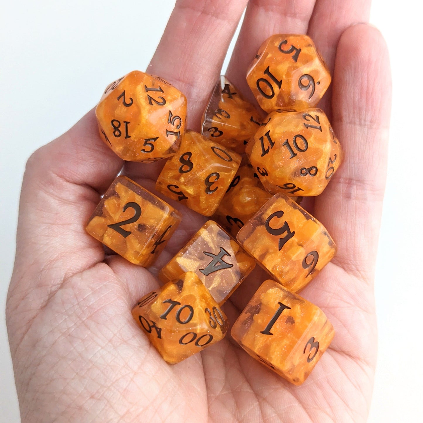 Hand holding orange Pumpkin Pie DnD dice set, perfect for cozy autumn gaming and fall campaigns.