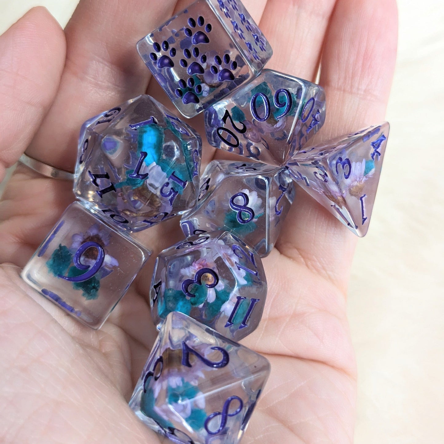Purple and blue floral DND dice set with paws on extra D6, held in hand. Fennek and Finch exclusive for tabletop RPGs.