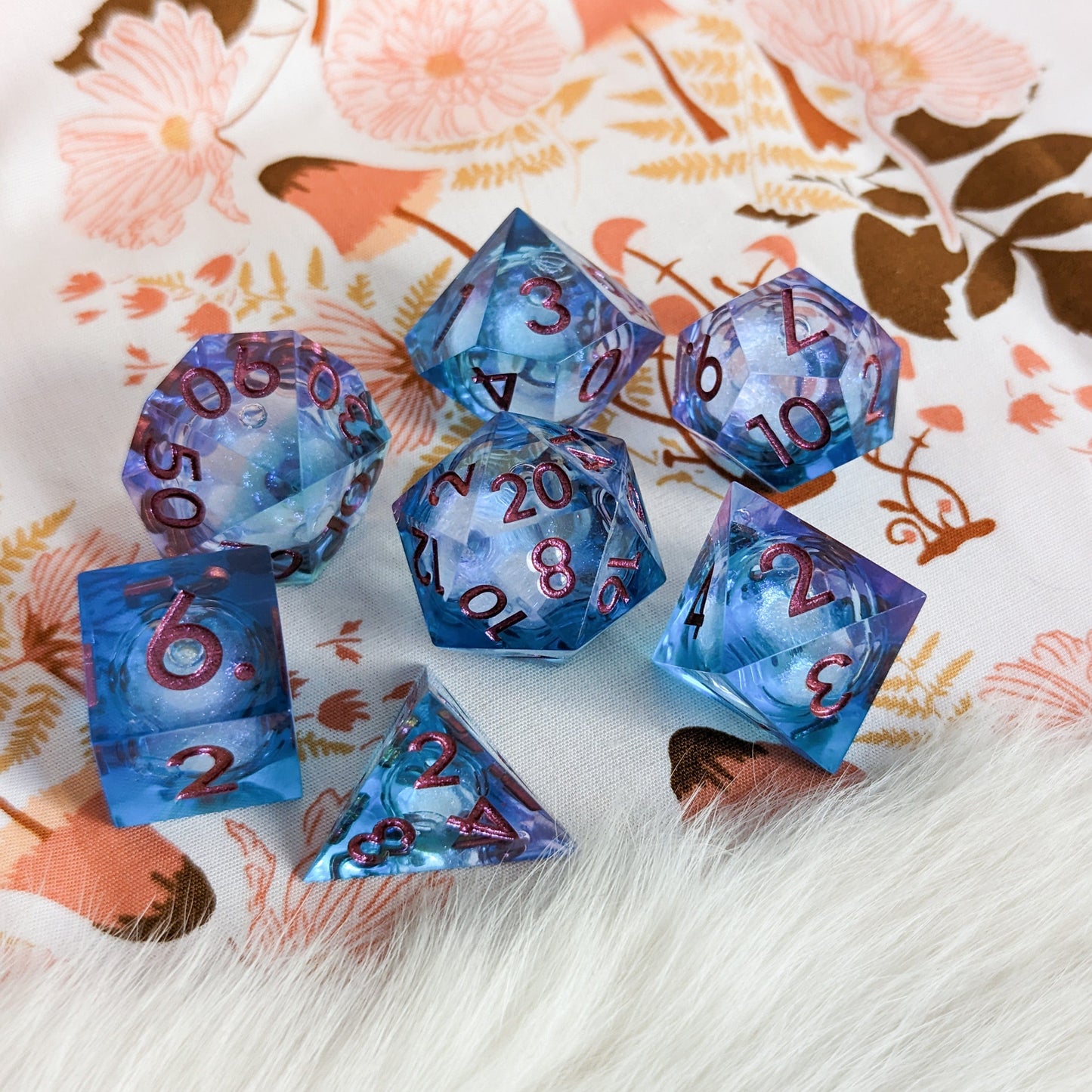 Purple and blue liquid core sharp edge resin DnD dice set with micro shimmer on floral fabric background.