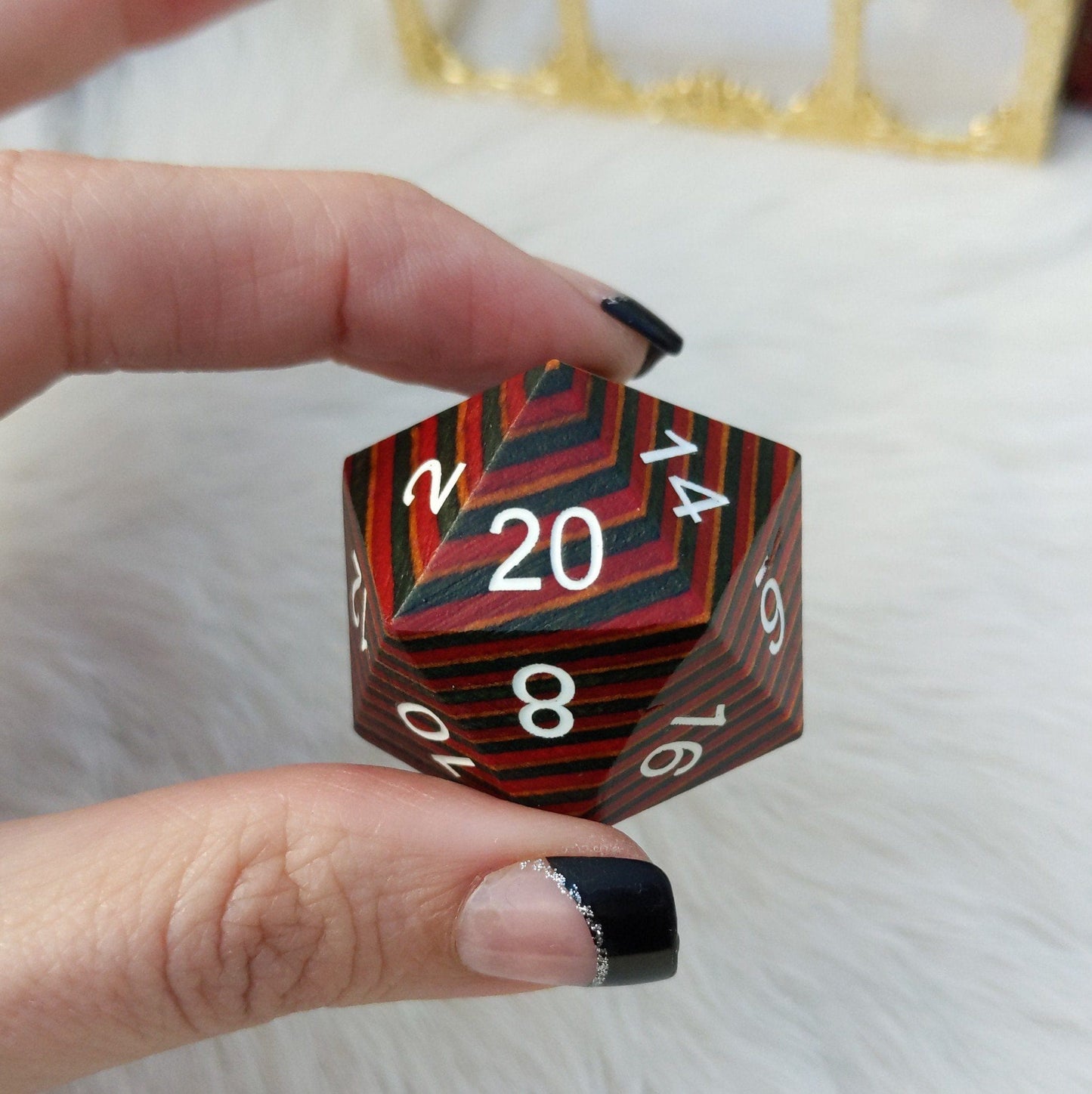 Hand holding a large red, blue, and brown stripe wooden D20 die with engraved numbers, perfect for collectors and gaming enthusiasts.