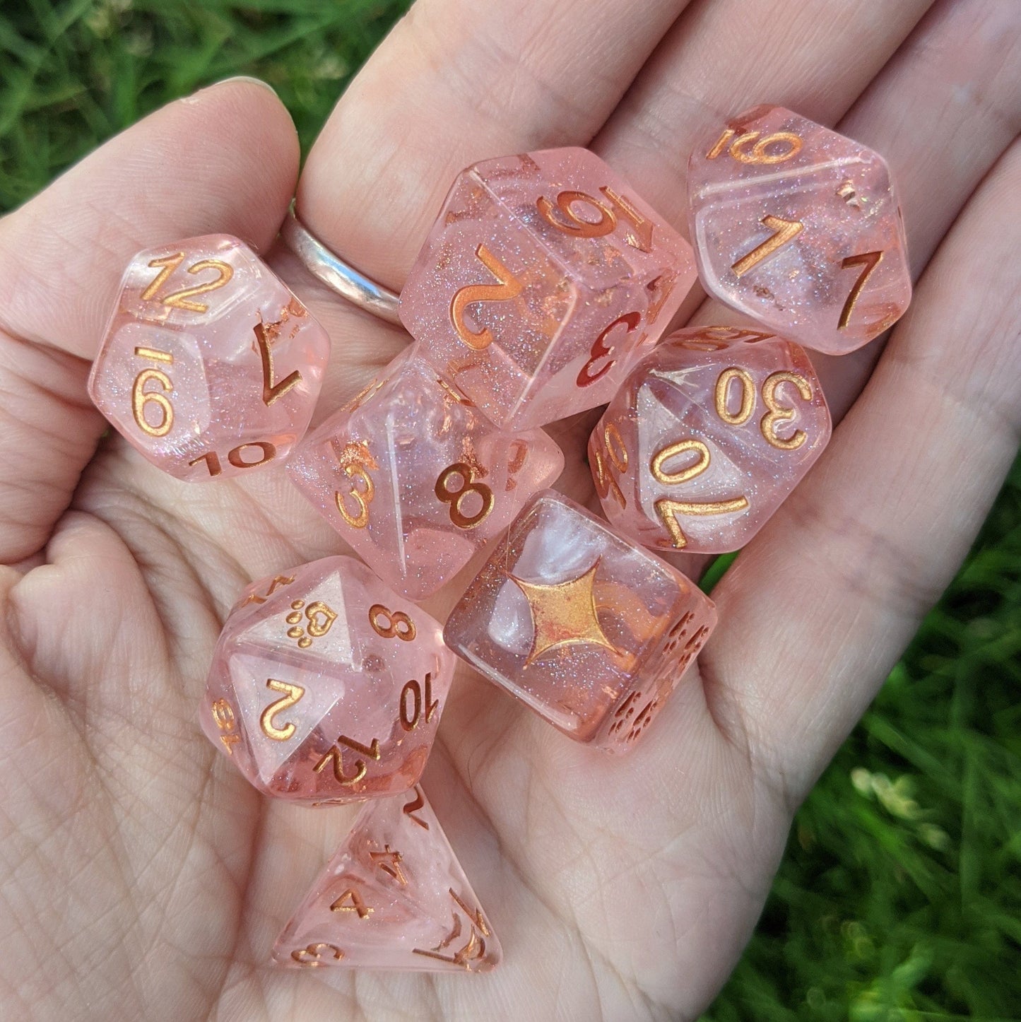 Sakura Cloud 8 Piece Dice Set in light clear pink, featuring pearly white clouds and copper foil, held in a hand on grass.