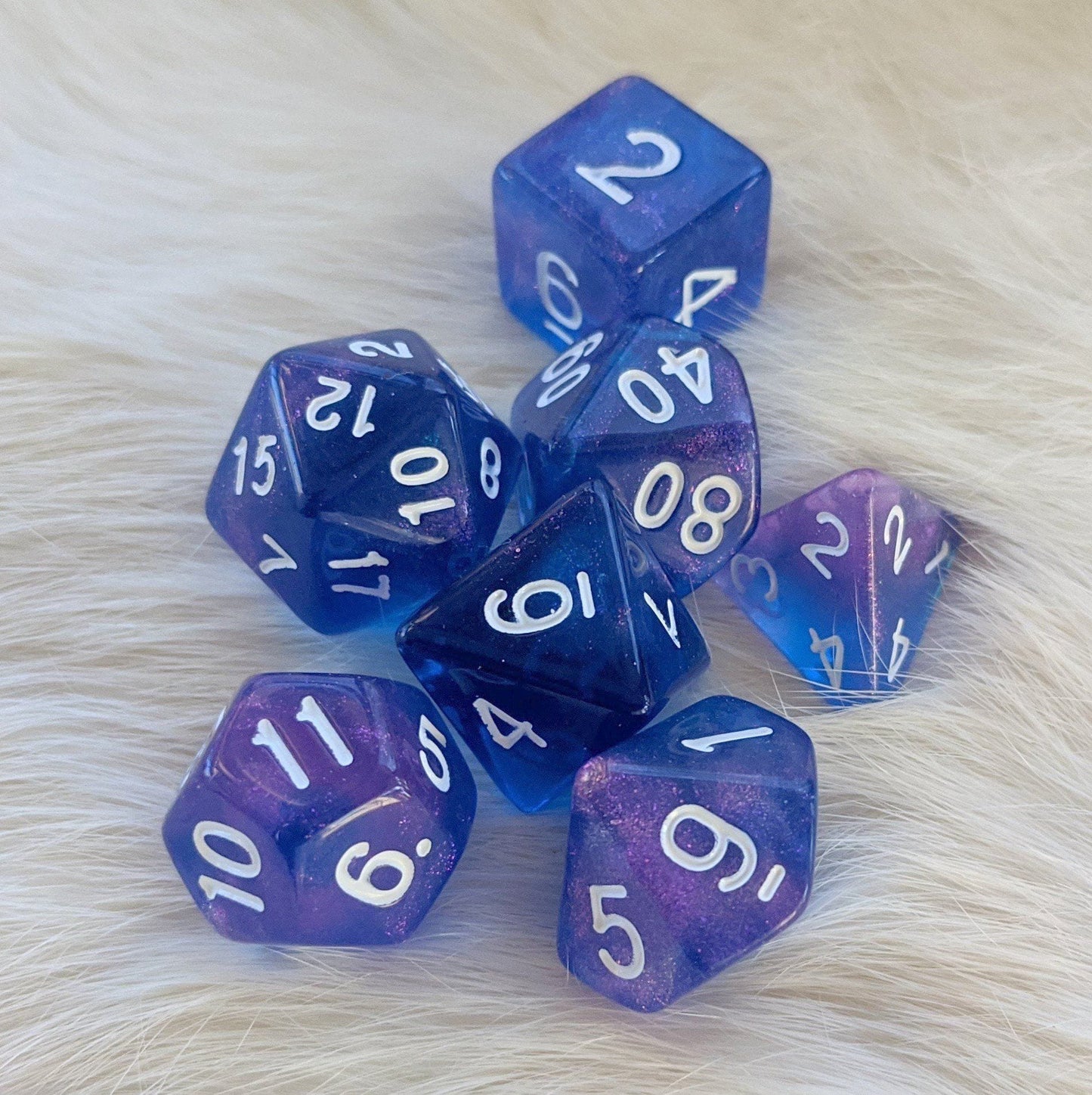Sapphire Phantom DnD Dice Set with marbled blue and purple shimmer and gold font on a fur background. 7 polyhedral dice for tabletop games.