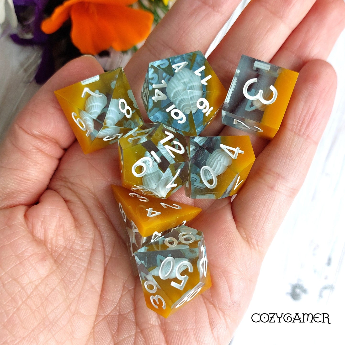 Hand holding 7-piece Sea Shell Sharp Edge Resin Dice Set with water and sand layers, perfect for DND and TTRPG gaming.