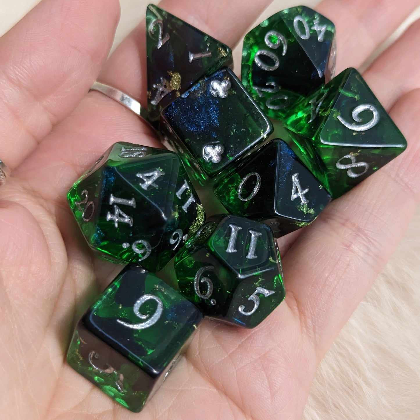 Hand holding Shadowy Forest DND dice set with green clear resin, black ink shimmer, and silver numbers.