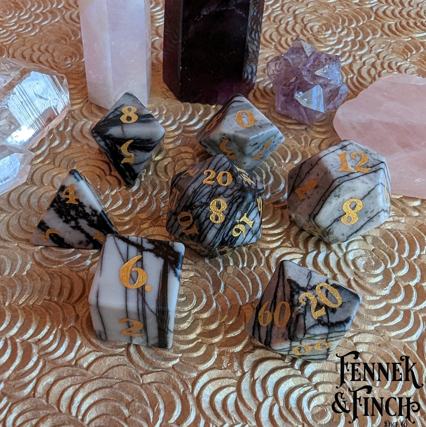 Spider Web Jasper gemstone dice set with gold numbers for tabletop RPG, surrounded by crystals on a textured surface.
