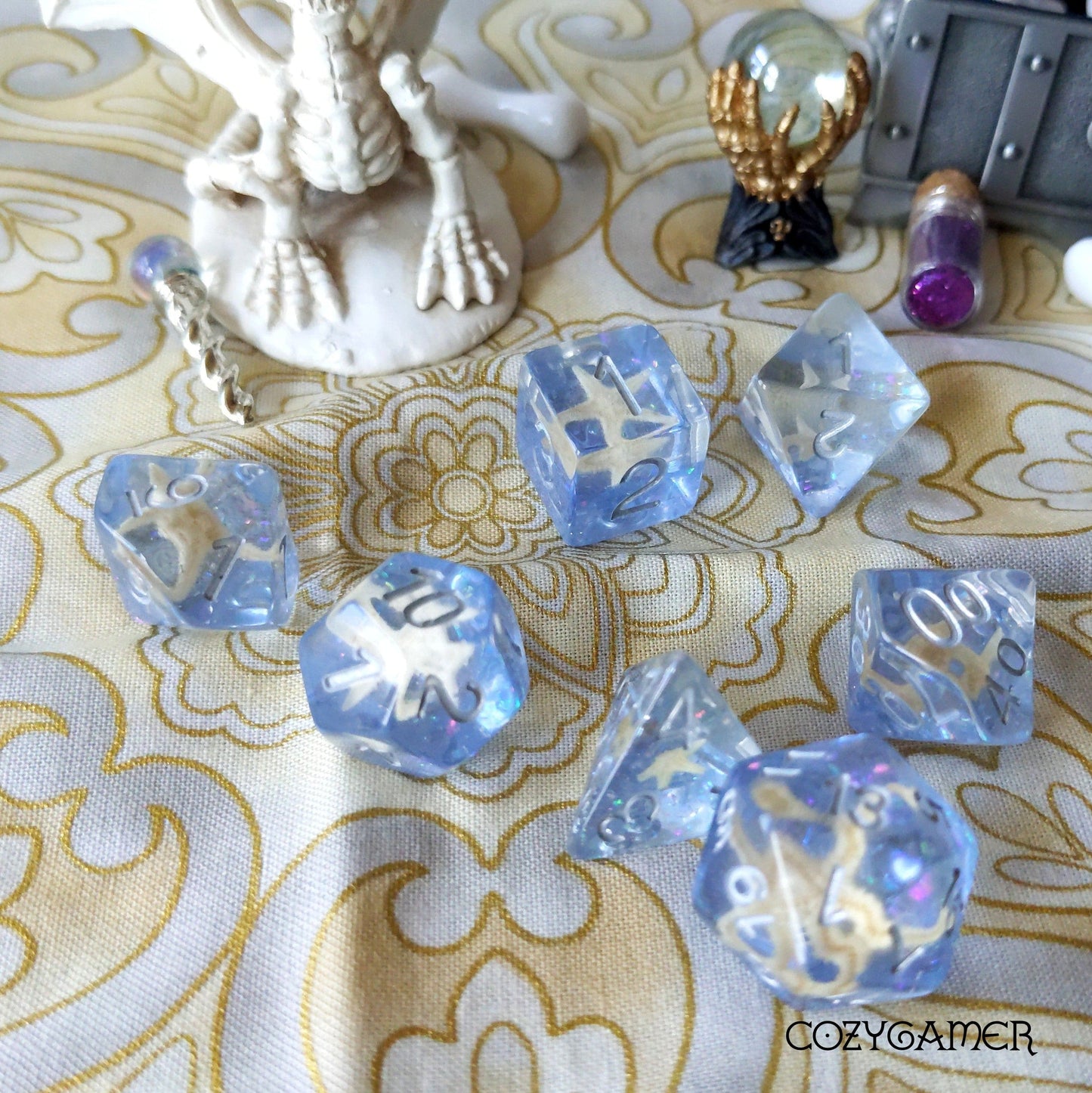 Starfish in Repose Dice Set with glittery periwinkle resin on patterned fabric, featuring TTRPG accessories and figurines.