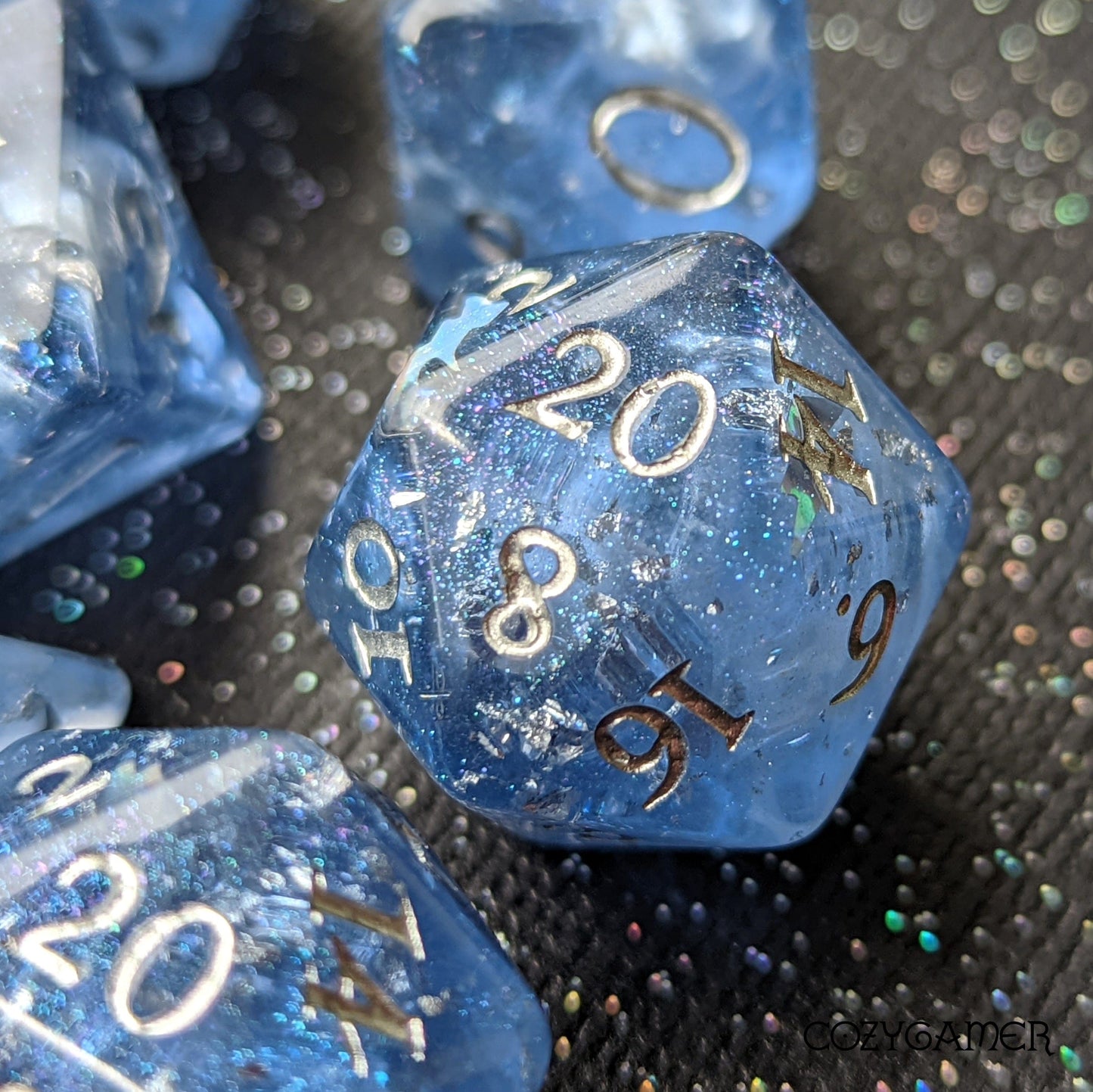 Blue Storm Daddy DnD dice set with white clouds, iridescent glitter, and silver numbers on a black surface. Perfect for tabletop gaming.