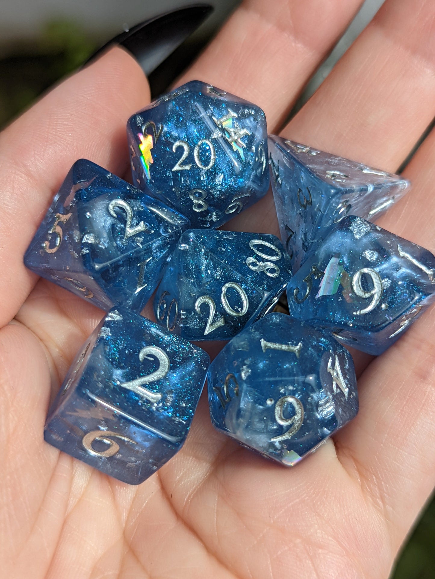 Hand holding Storm Daddy DnD dice set in blue with silver numbers, featuring glitter and holographic lightning for tabletop games.