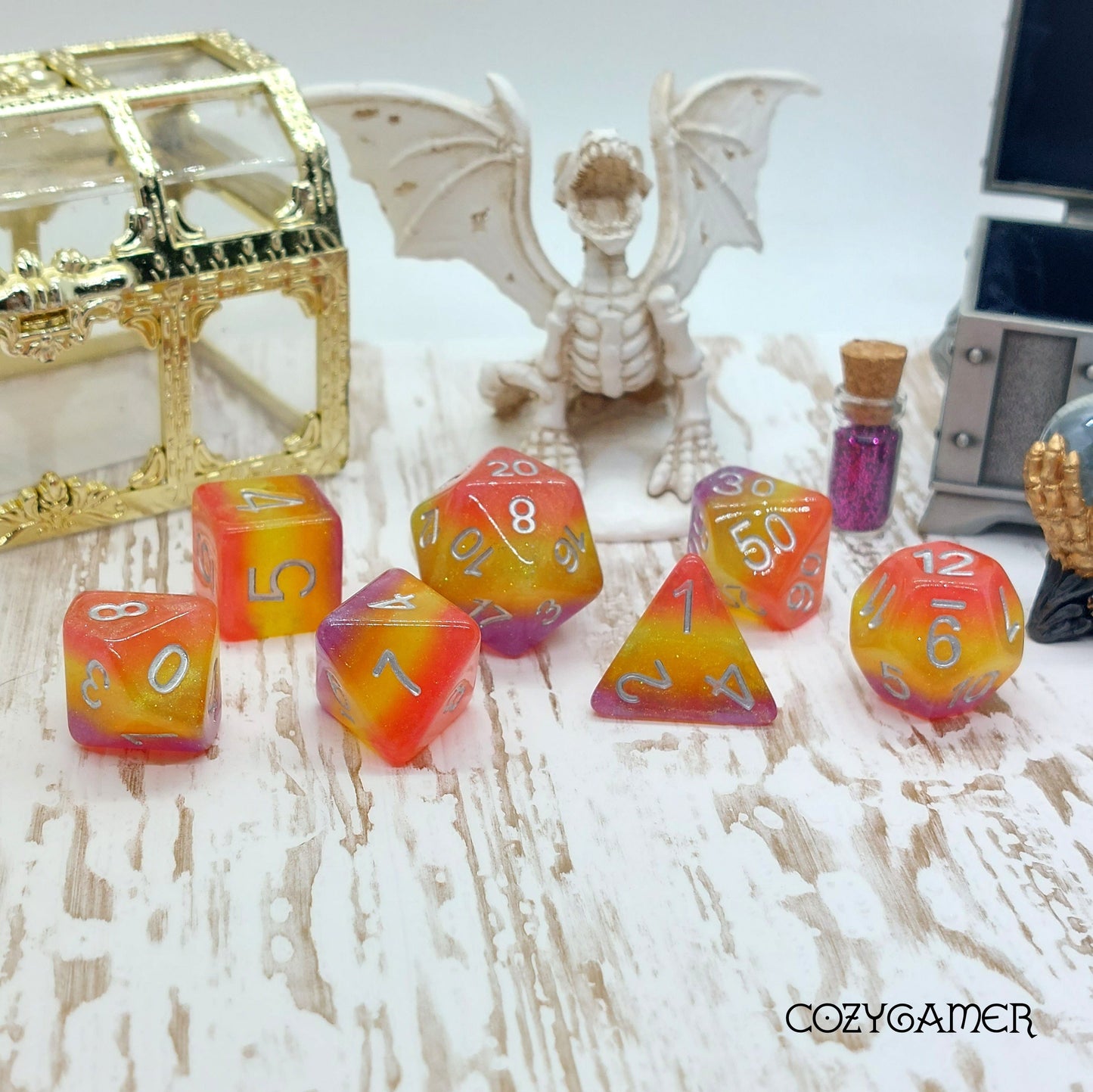 Summer Sunset Dice Set with layered glitter in bright colors, 7 polyhedral pieces for DnD, displayed with fantasy decor.