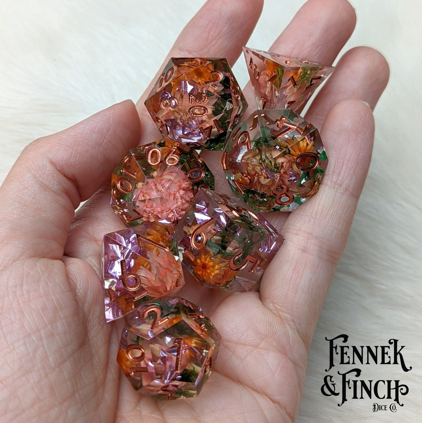 Hand holds Sunny Garden DnD dice set with dried orange and pink flowers inside, featuring sharp edges and hand-finished design.