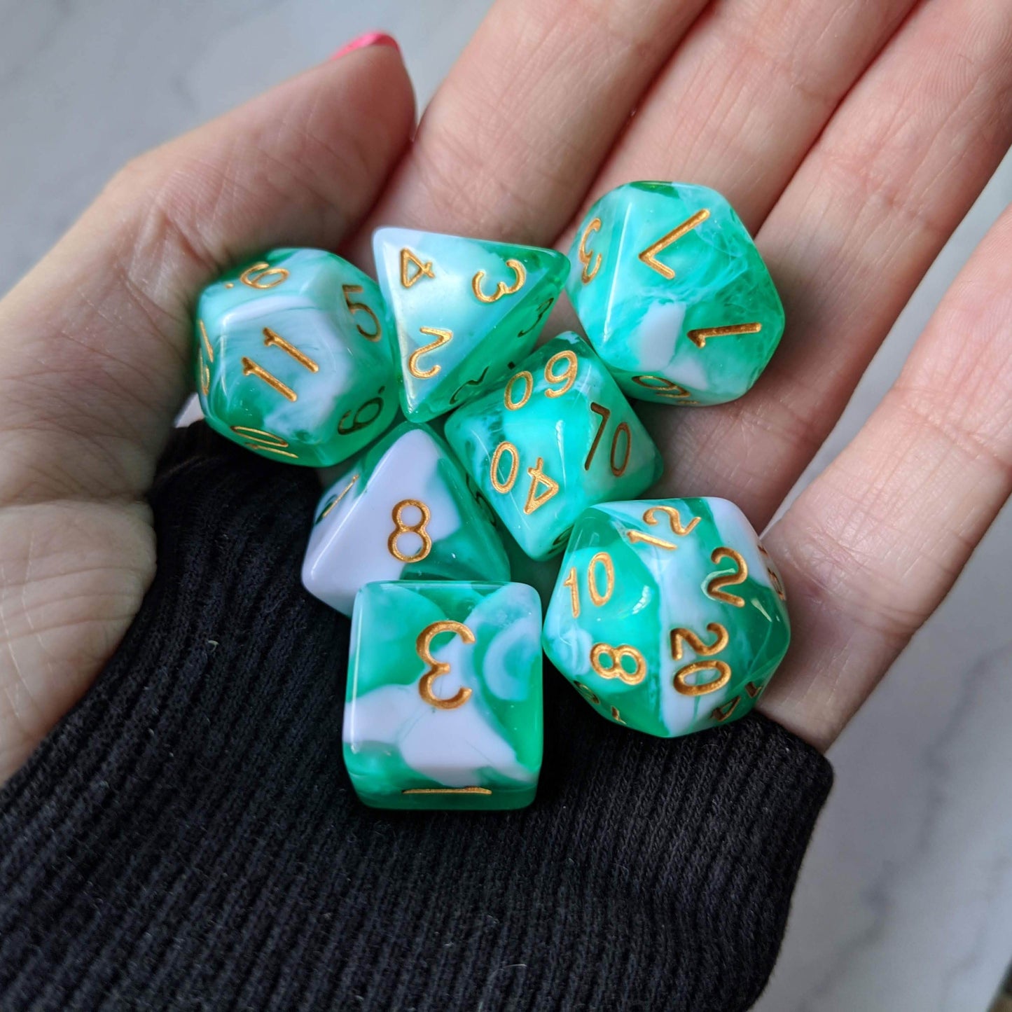 Teal and white marbled dice set with gold numbers, perfect for tabletop RPGs like Dungeons and Dragons, held in hand.