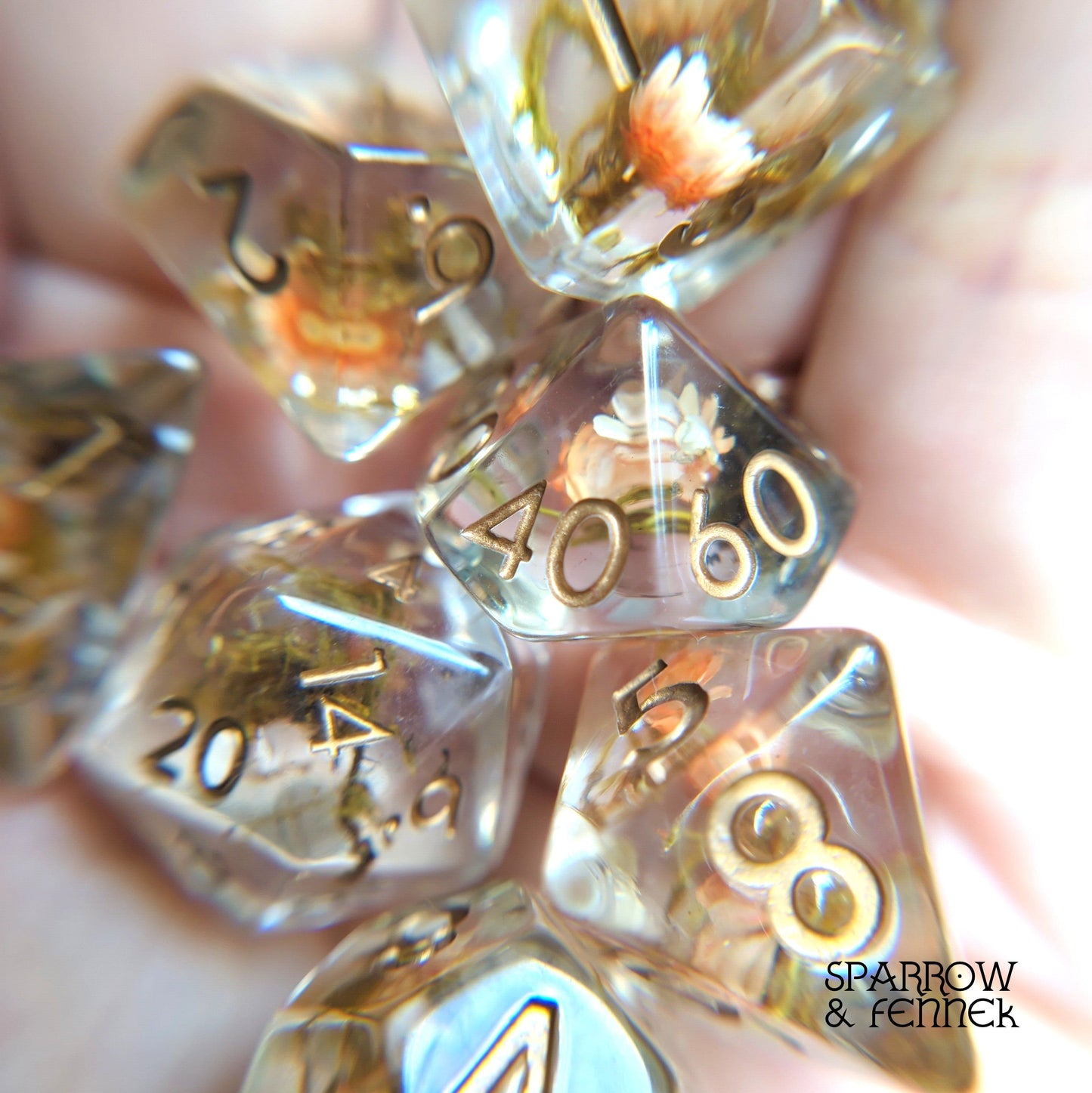 Close-up of a resin dice set with tiny orange flowers and moss inside, designed for Dungeons and Dragons and other tabletop games.