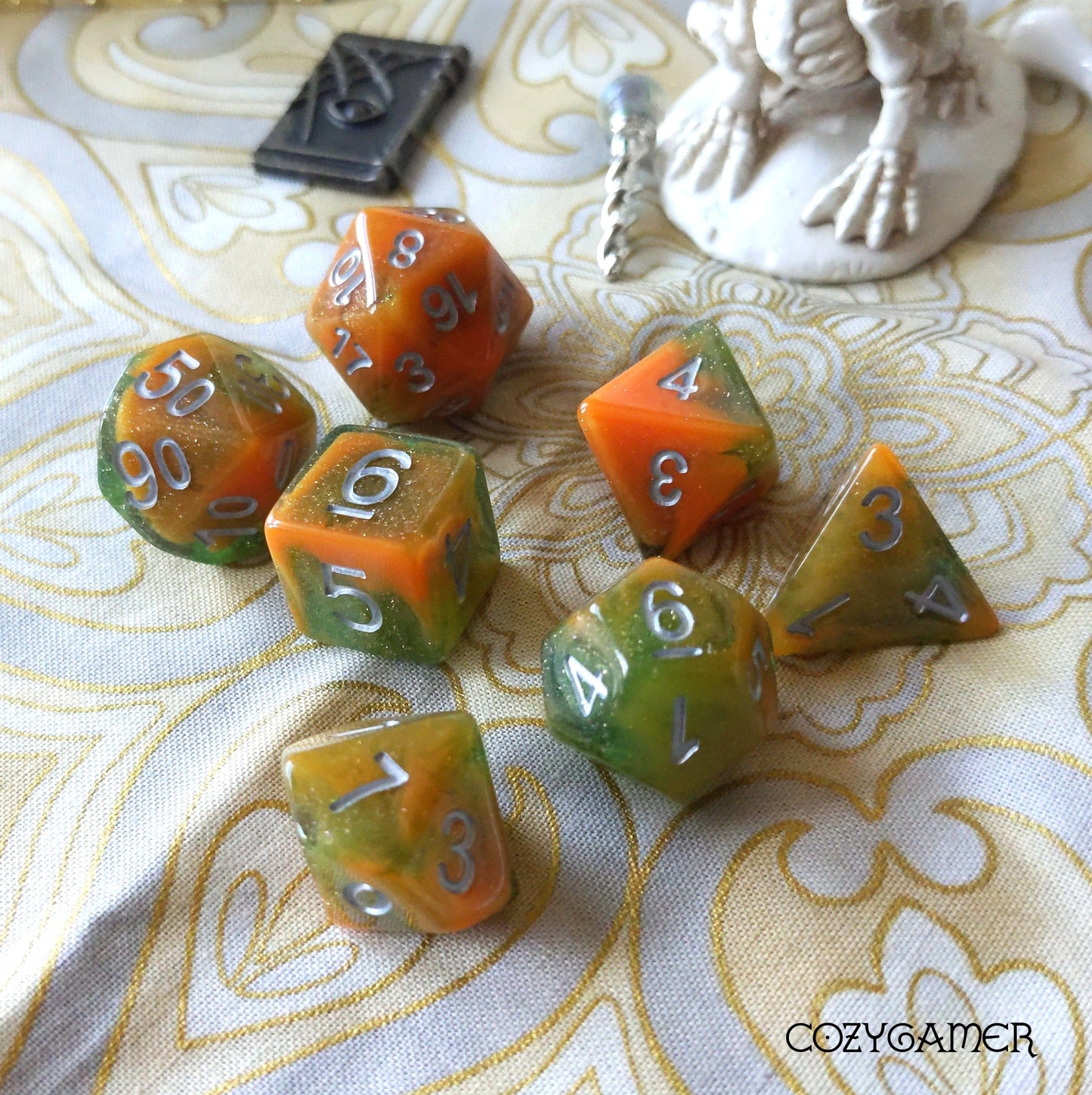 Orange and green Toxins Dice Set with 7 polyhedral dice for tabletop RPGs on a decorative cloth background.