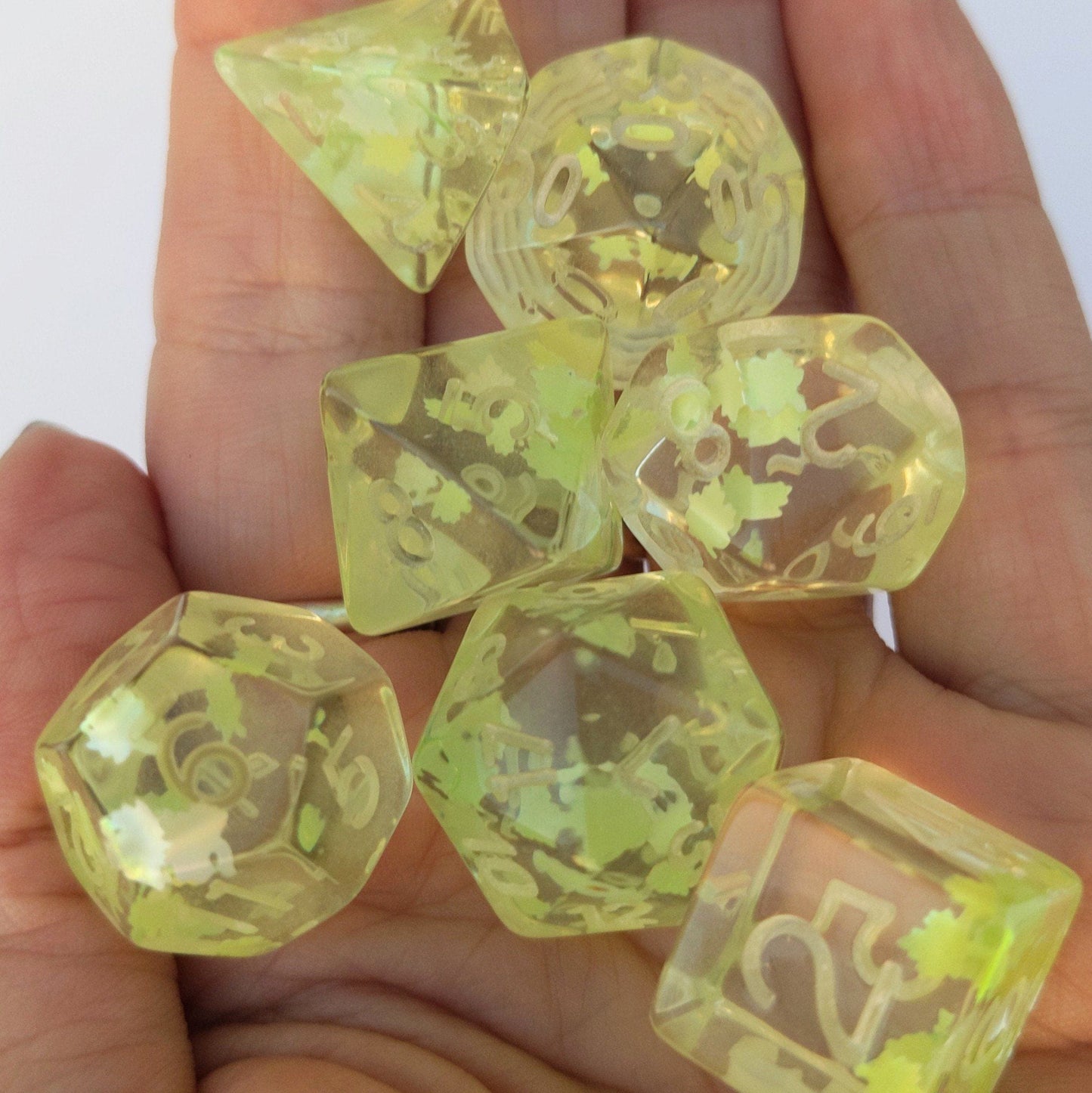 Un-inked Feywild Dice Set in clear resin with light green leaves on hand, ideal for Dungeons and Dragons and Magic The Gathering games.