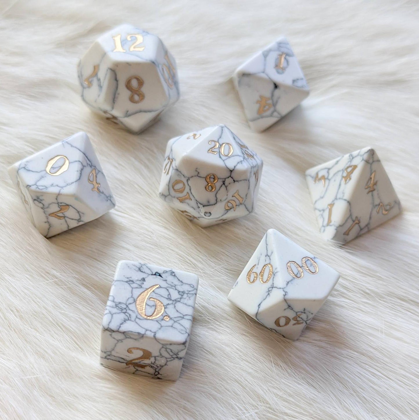 White Howlite gemstone dice set on a soft surface, featuring intricately carved numbers and a marble-like pattern.
