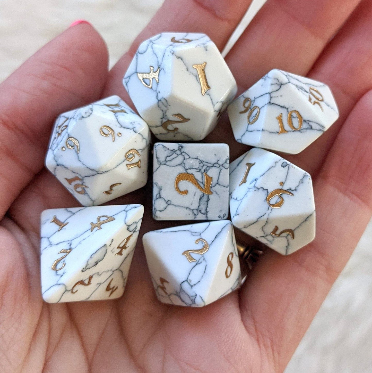 White Howlite gemstone dice set with gold numbers, TTRPG seven-piece set in hand, showcasing exquisite craftsmanship and durability.