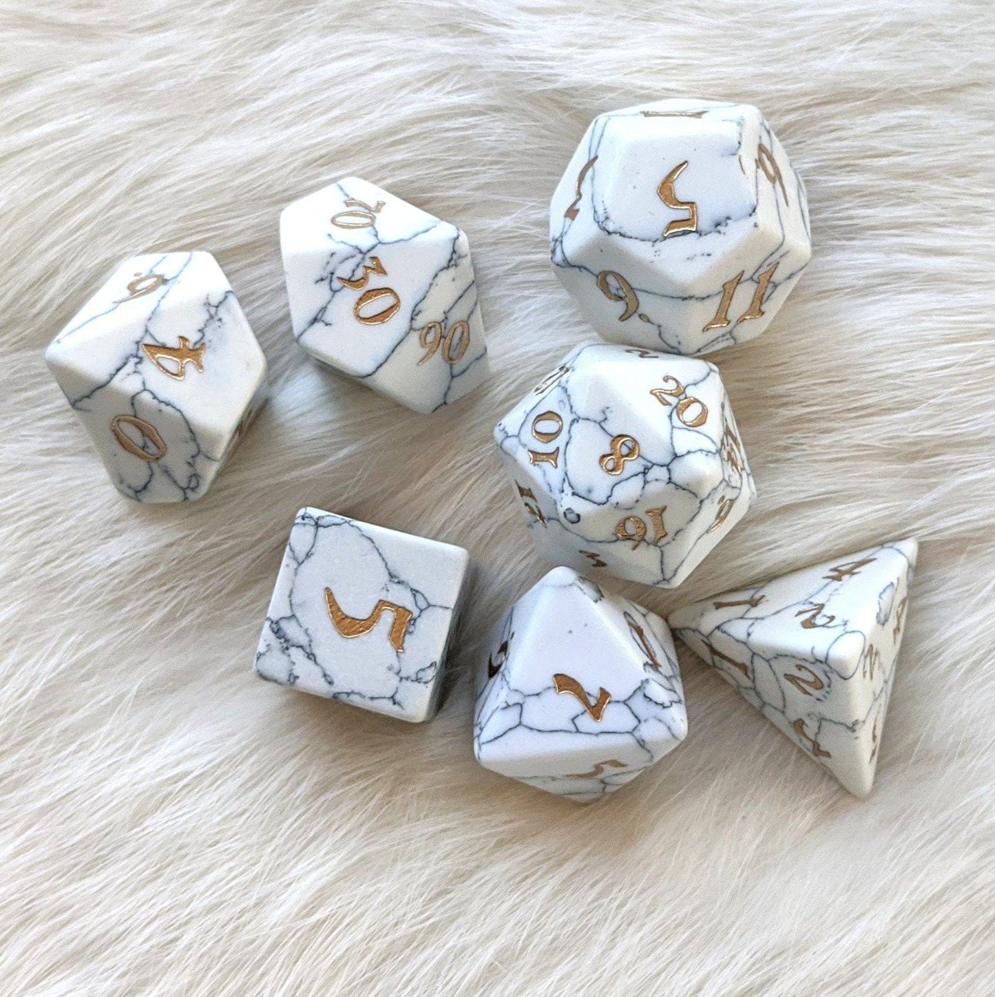 White Howlite gemstone TTRPG dice set with gold numerals on a white fur background, 7-piece polyhedral dice.