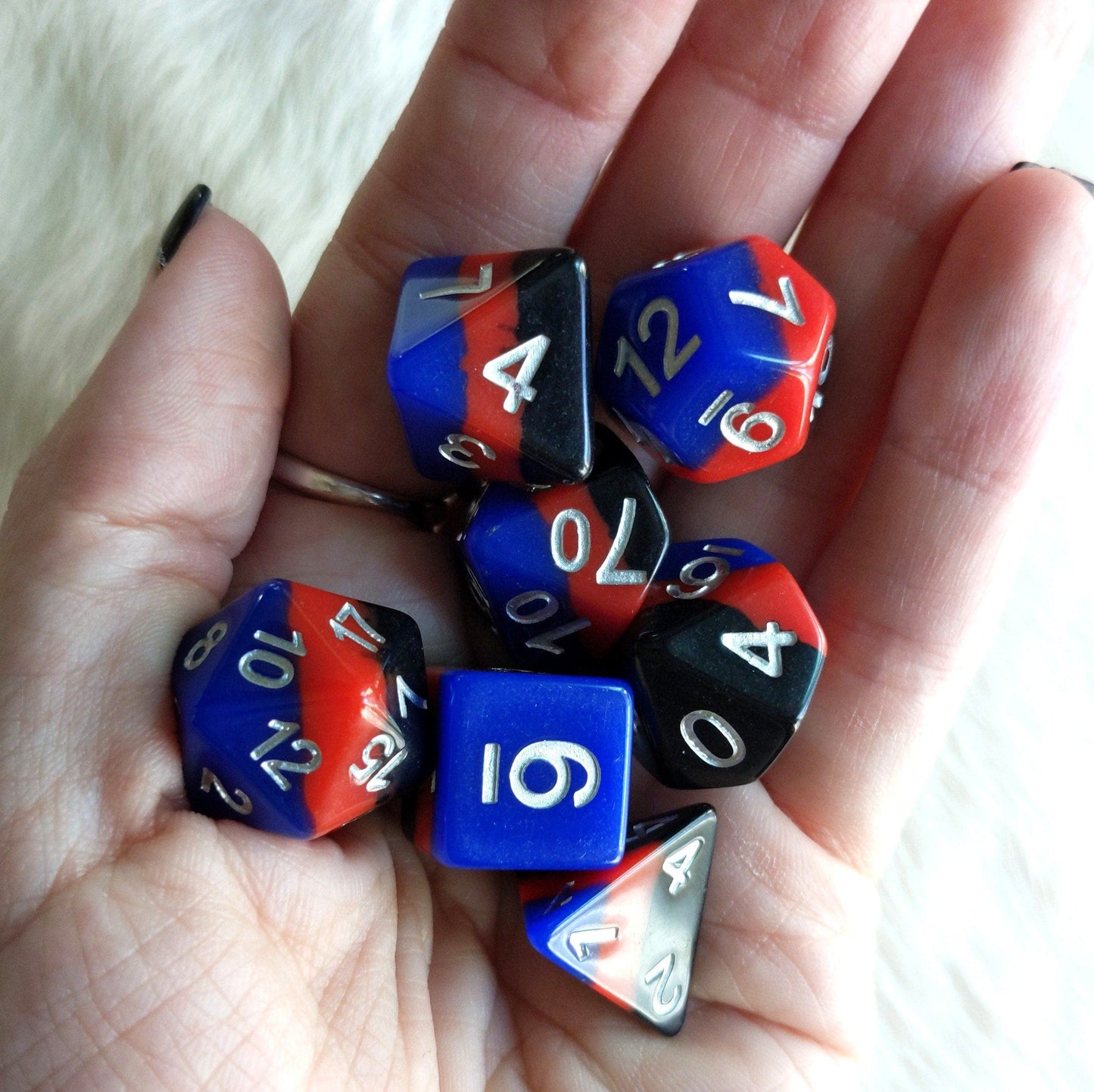 Hand holding Windsor Castle Dice Set in black, red, and blue with silver numbers for tabletop RPGs like Dungeons and Dragons.