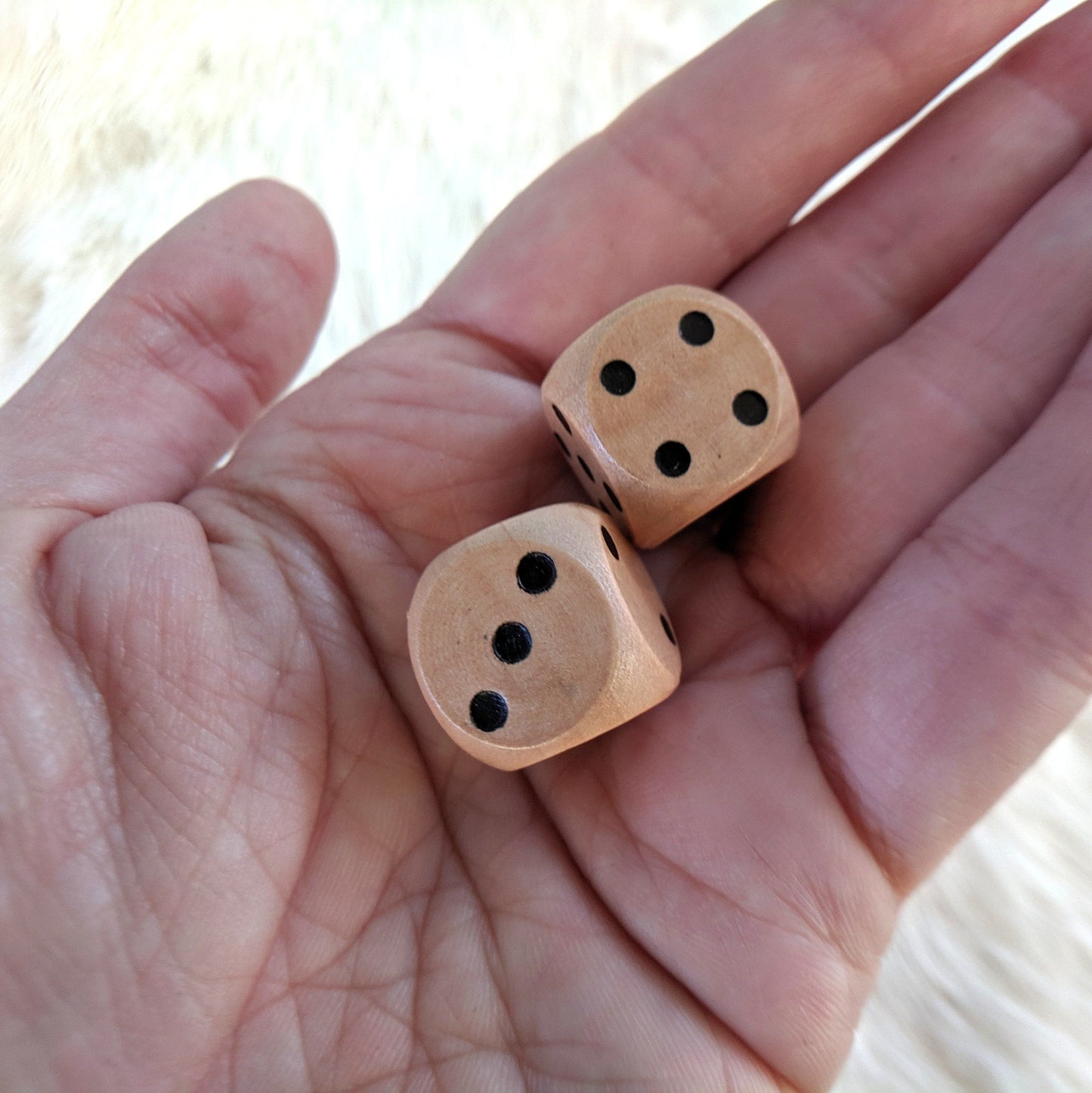 Hand holding light wooden dice set of 2 D6s, perfect for gift or collection.