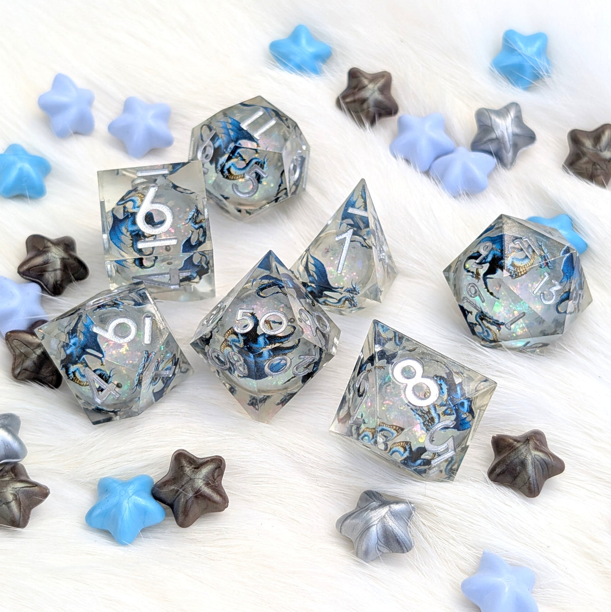 A set of clear acrylic polyhedral dice with blue and black marbled swirls, scattered on a white faux fur background with blue, gray, and brown star-shaped decorative pieces.