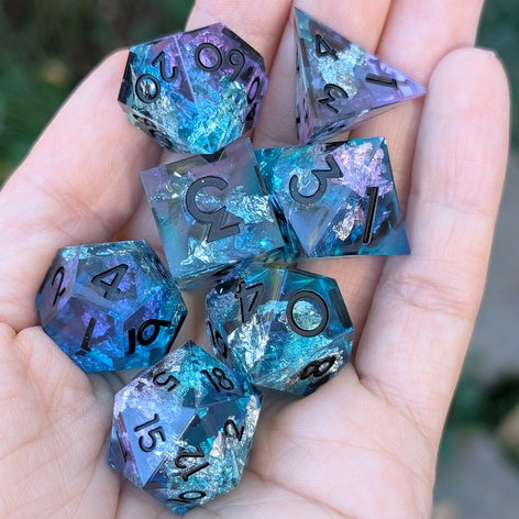 A set of seven translucent blue and purple resin polyhedral gaming dice with black printed numbers, held in a person's hand.