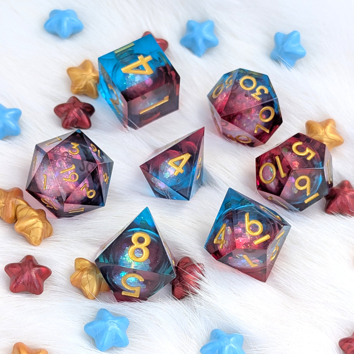 A set of translucent polyhedral gaming dice with a blue-to-purple iridescent gradient and gold numbers, arranged on a white faux-fur surface with scattered blue, gold, and red star-shaped props.