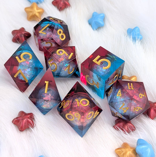 A set of translucent polyhedral gaming dice with gold numbers, arranged on a white faux fur surface with colorful star-shaped props. The dice feature a cosmic blue and red nebula design with glitter.