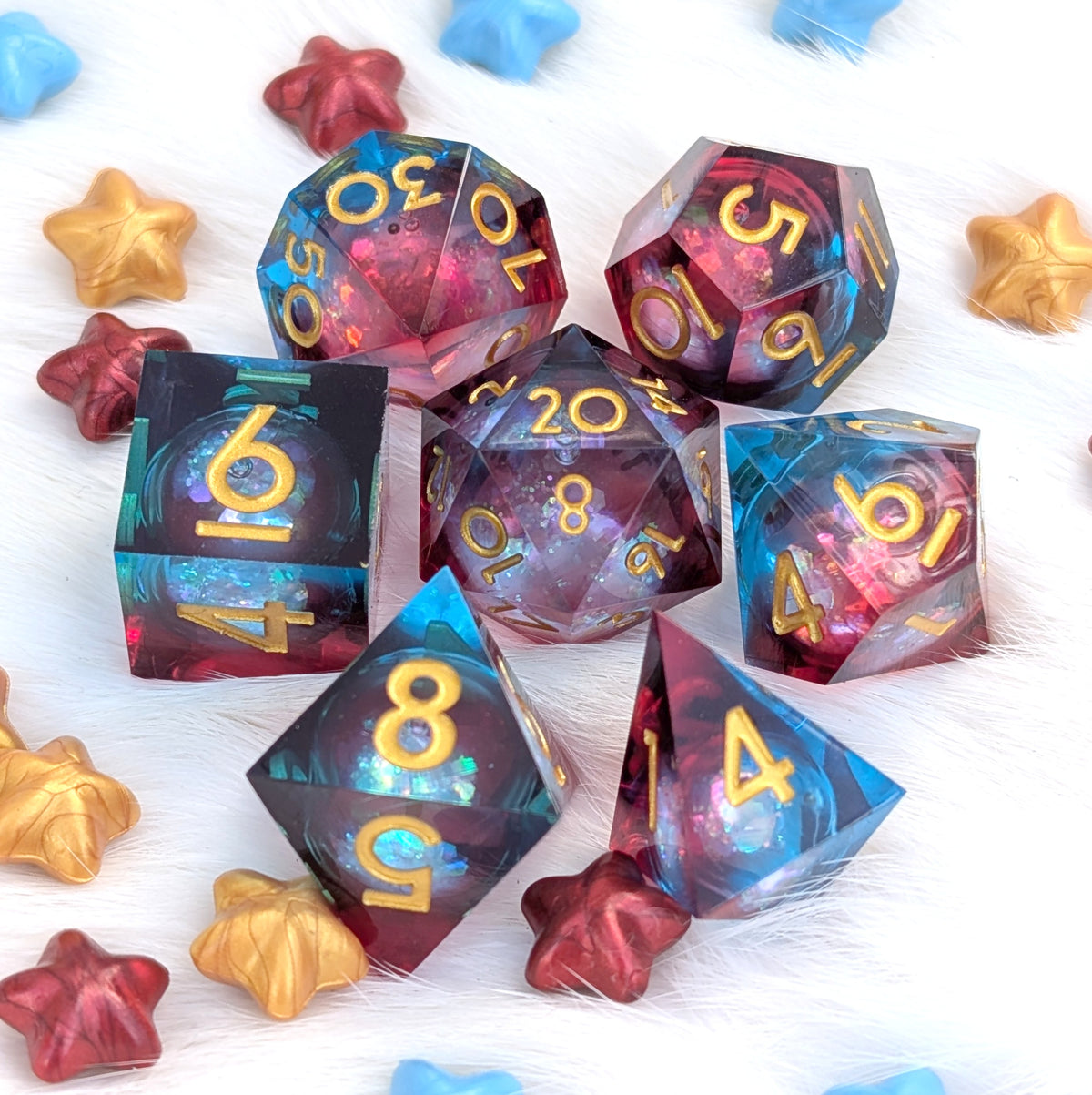 A set of translucent polyhedral gaming dice with gold numbers, arranged on a white faux-fur surface with small star-shaped decorative props. The dice show a swirling galaxy-like pattern in blue, purple, and pink tones.
