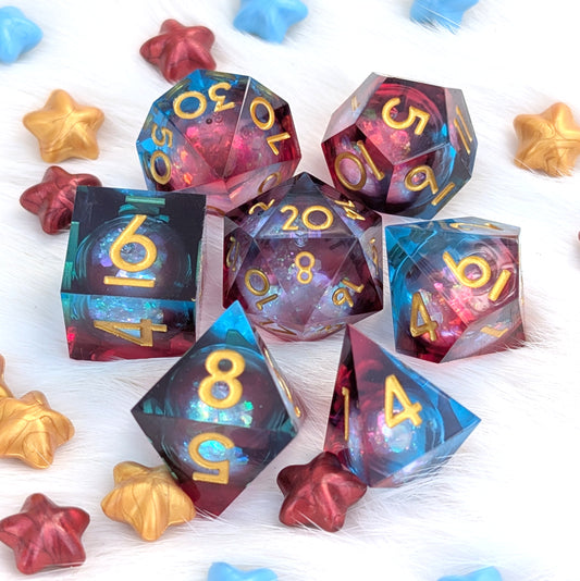 A set of translucent polyhedral gaming dice with gold numbers, arranged on a white faux-fur surface with small star-shaped decorative props. The dice show a swirling galaxy-like pattern in blue, purple, and pink tones.