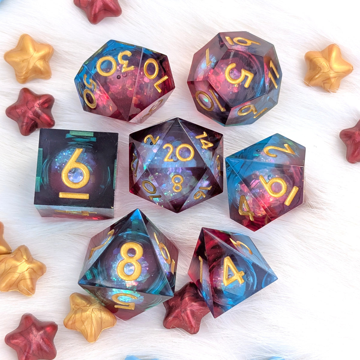A set of holographic polyhedral dice with gold numbers, arranged on a white faux fur background with decorative red and gold star-shaped props.