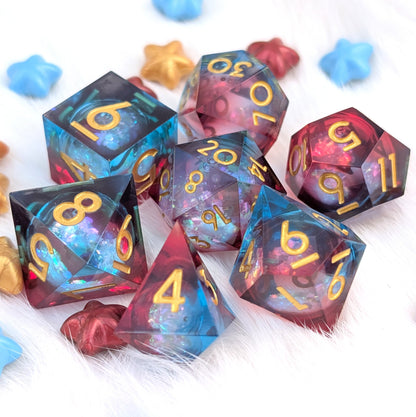 A set of translucent polyhedral dice with a galaxy-like blue, purple, and pink internal pattern and gold numbers, arranged on a white furry surface with small star-shaped confetti.