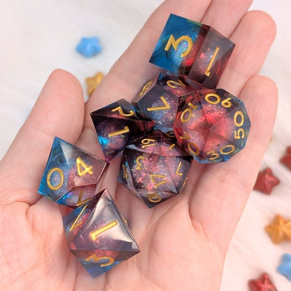 A set of translucent polyhedral gaming dice with gold numbers, displayed in a person's hand. The dice feature a cosmic galaxy design with blue, purple, and red nebulae and gold glitter.