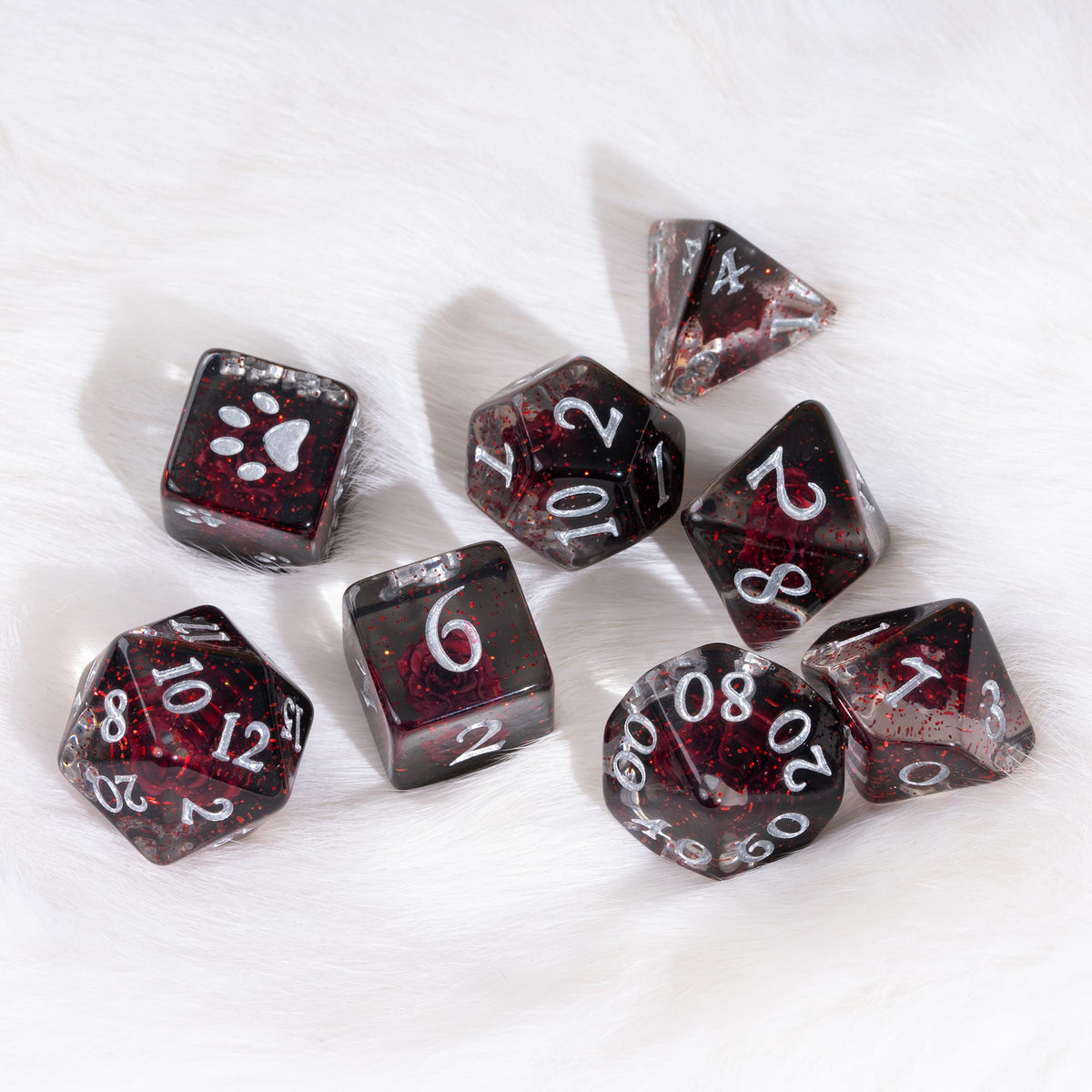 A set of translucent dark red and black polyhedral dice with white printed numbers and symbols, arranged on a white faux fur background.