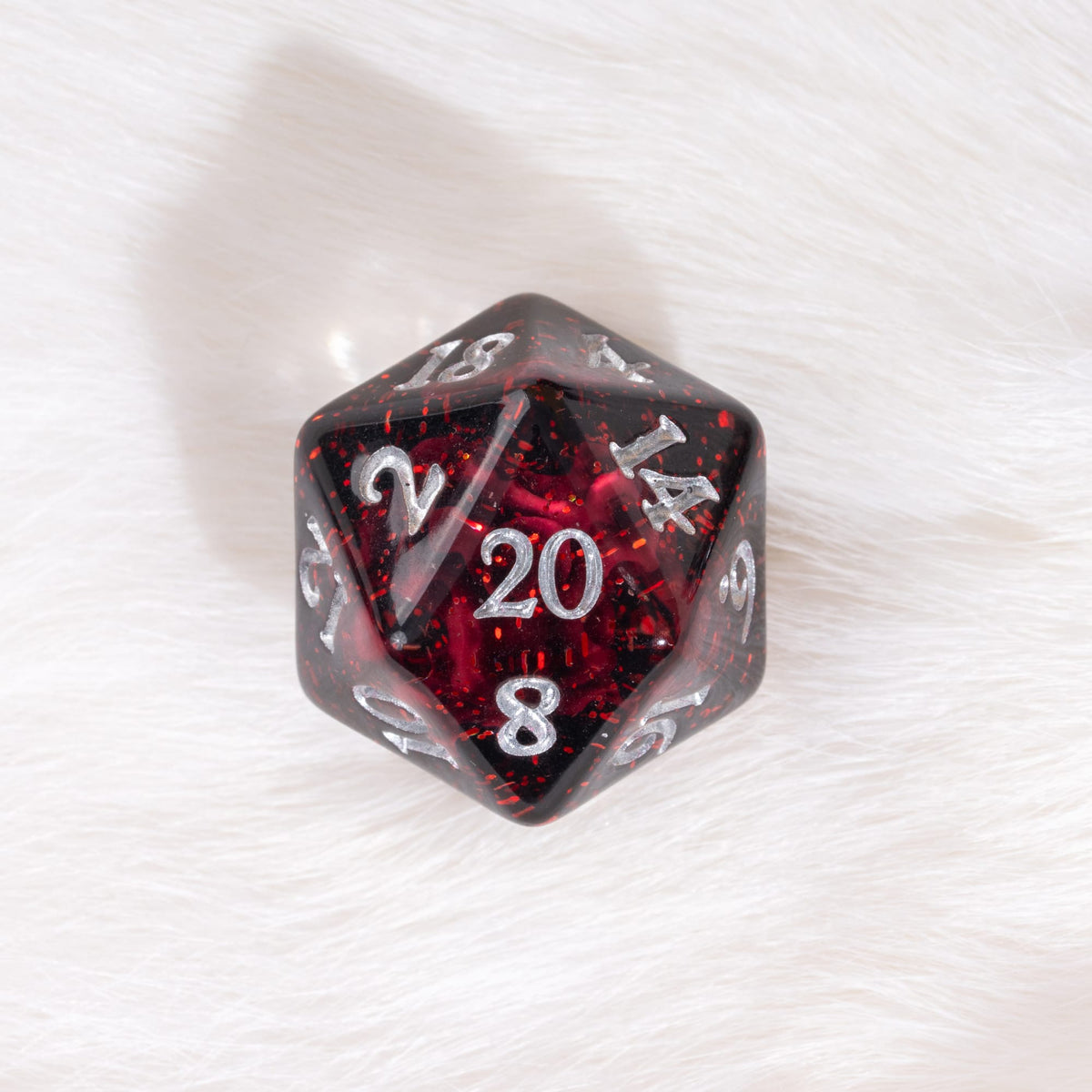 A red glittery 20-sided d20 die with silver numbering, resting on a white faux fur surface.