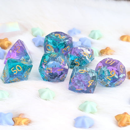 A set of holographic polyhedral gaming dice in pastel rainbow colors with gold numbering, arranged on a white faux fur surface with scattered pastel star-shaped confetti.