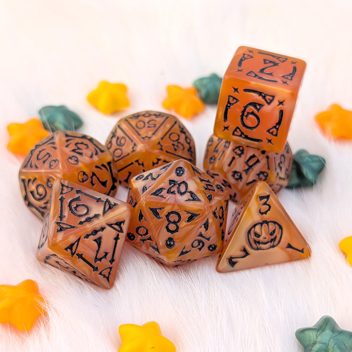 Haunted Harvest Halloween acrylic DnD dice with pearly marbled pumpkin-orange coloring, black numbers, and illustrations of ghosts, bats, broomsticks, skulls, bones, and jack-o'-lanterns