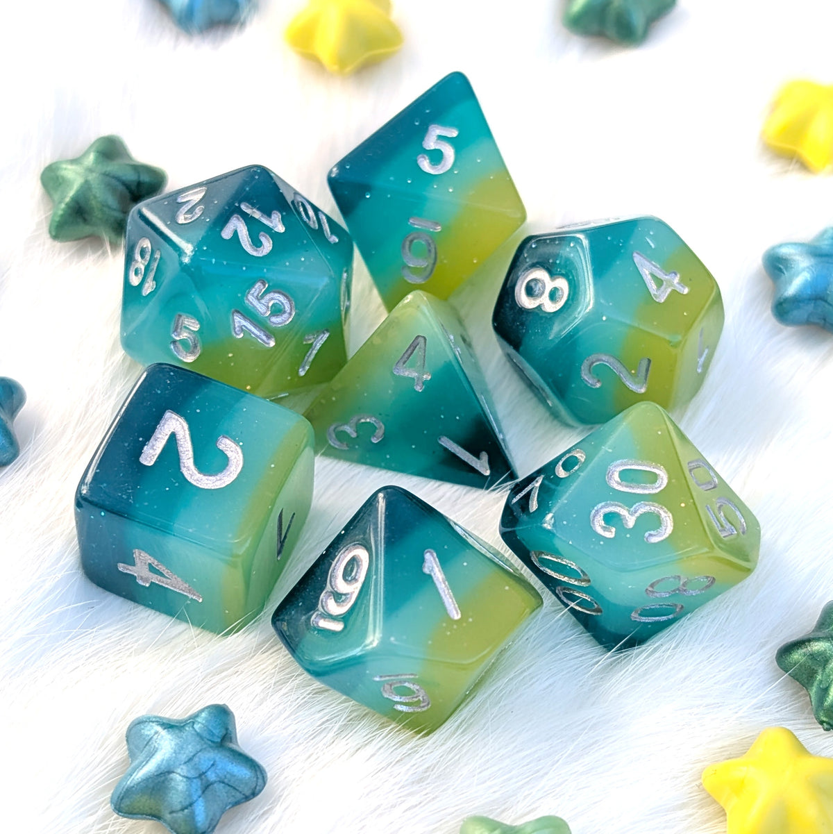 Lagoon Dreams 7-piece round-edge resin DnD dice with glittering kiwi green, light blue, teal, and deep teal layers and silver numbers