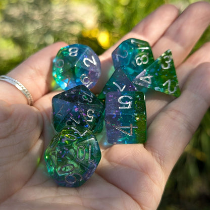 Aurora Sparkle Dice Set, green, blue, purple hues with iridescent glitter, held in a hand, inspired by northern lights, RPG accessory.