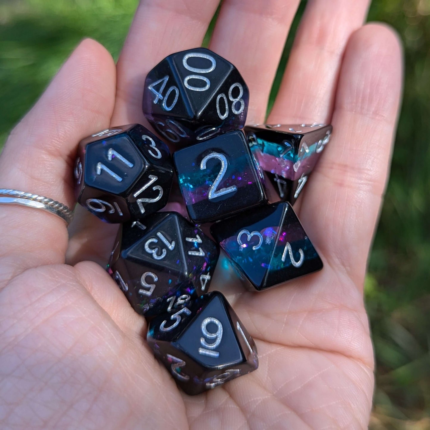 Hand holding Midnight Nebula dice set with round edges, featuring black layers and a sparkling blue and purple core.