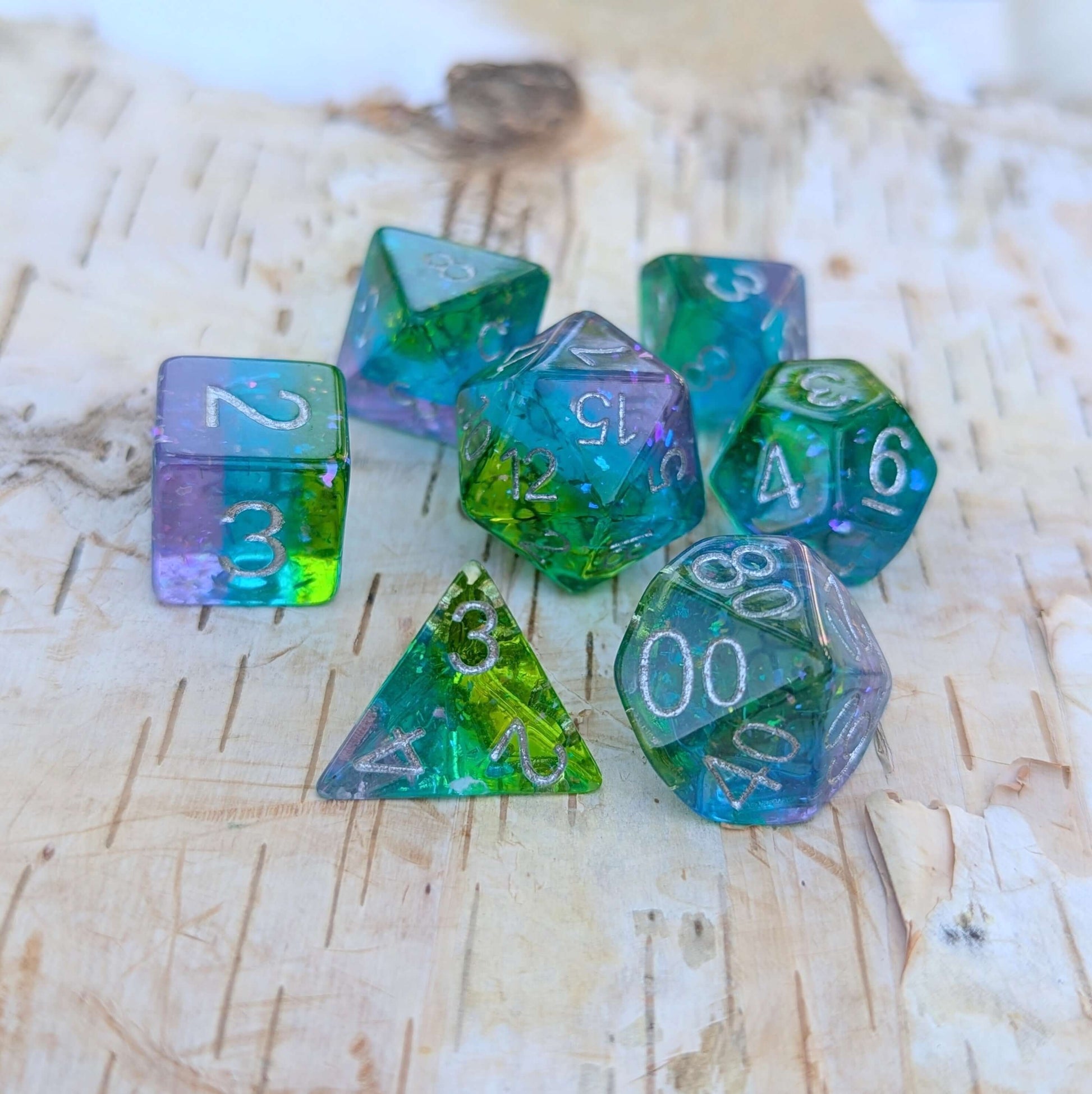 Aurora Sparkle Dice Set with glittering green, blue, and purple hues on a wooden background.