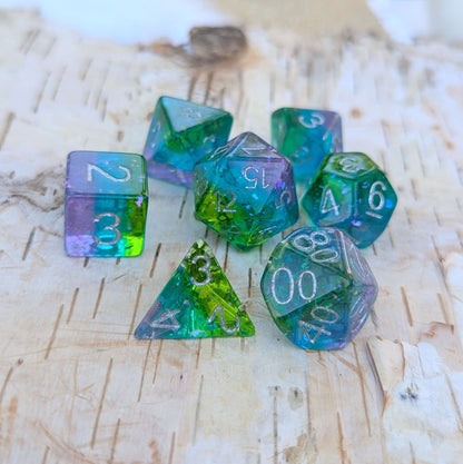 Aurora Sparkle Dice Set with glittering green, blue, and purple hues on a wooden background.