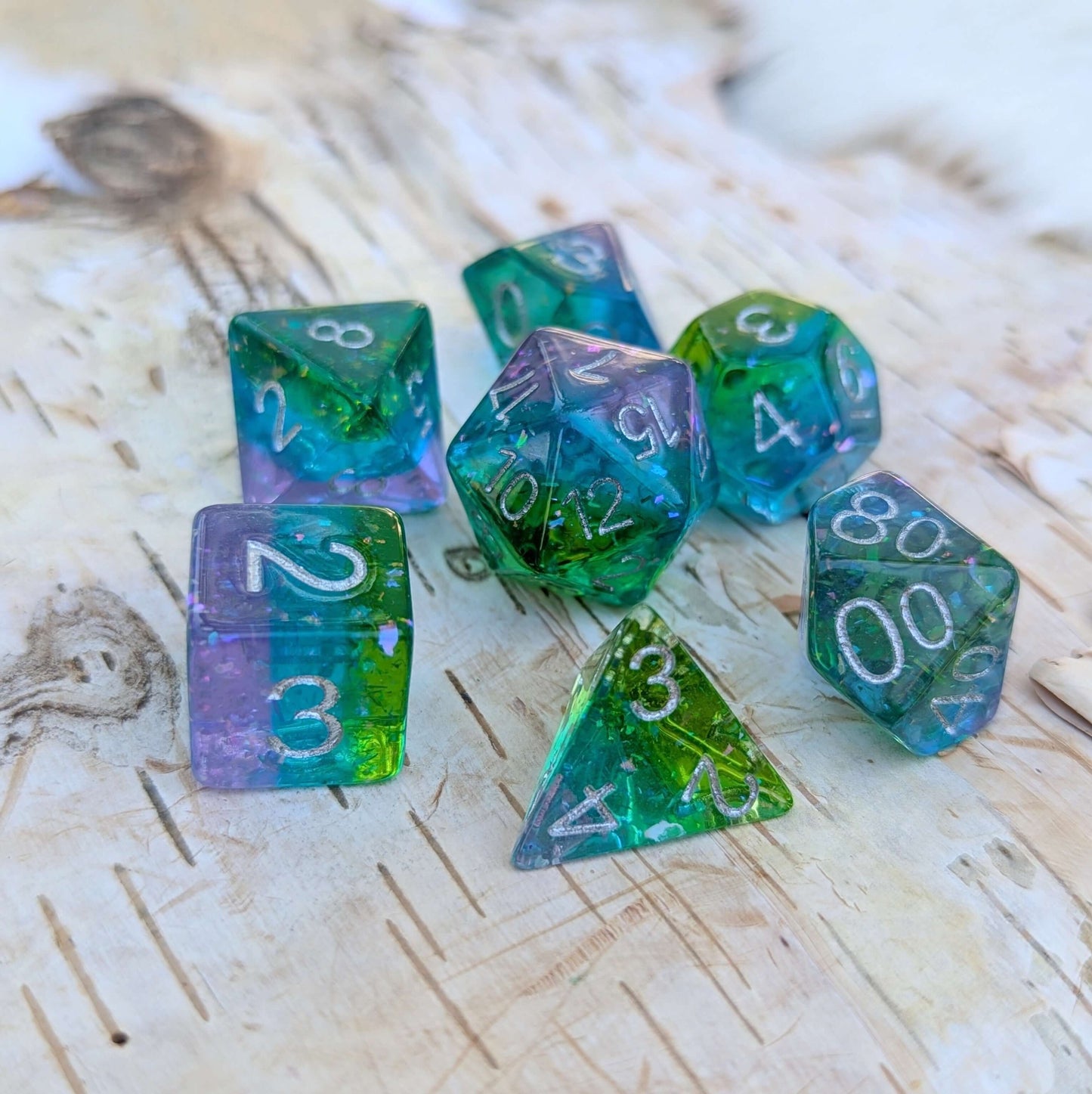 Aurora Sparkle Dice Set with layered green, blue, and purple colors, featuring glitter flakes, on a wooden background.